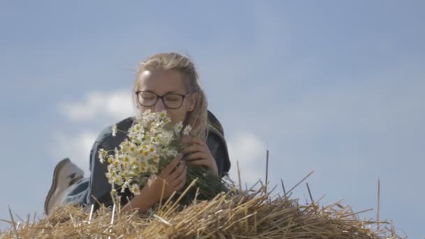 Ragazza sdraiata su una pila di paglia con un bouquet di margherite bianche — Video Stock