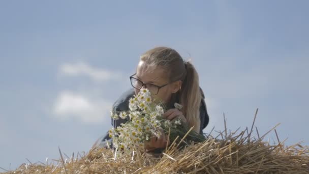 Girl lying on a stack of straw with a bouquet of white daisies — Stock Video