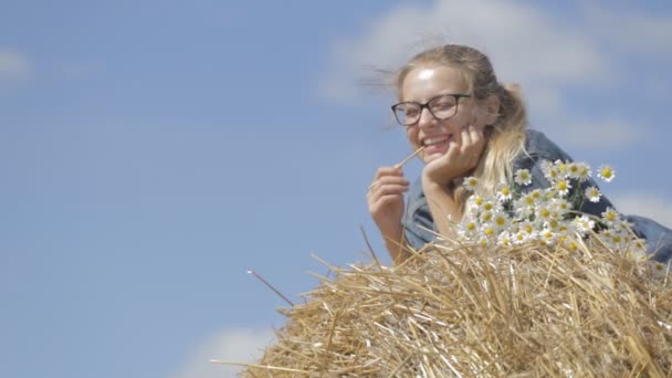 Chica acostada en una pila de paja con un ramo de margaritas blancas — Vídeos de Stock