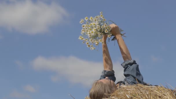 Meisje liggend op een stapel van stro met een boeket van witte madeliefjes — Stockvideo