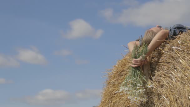 Fille couchée sur une pile de paille avec un bouquet de marguerites blanches — Video