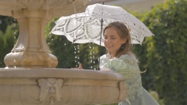 Chica con un paraguas blanco en la fuente — Vídeo de stock