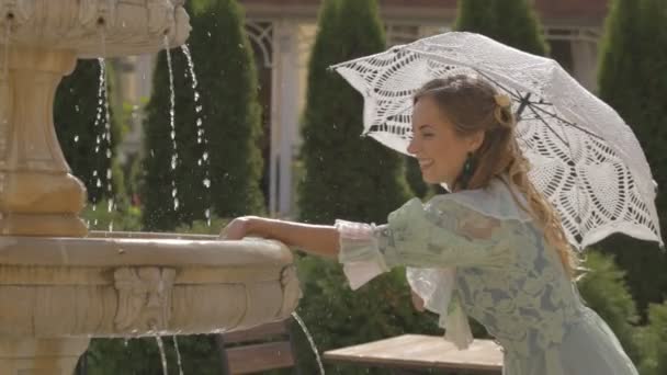 Mädchen mit weißem Regenschirm am Brunnen — Stockvideo