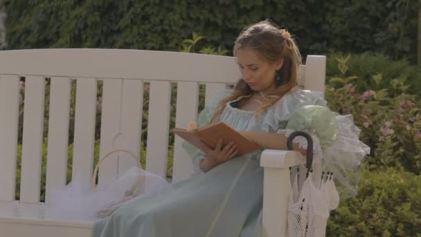 Chica en un banco leyendo un libro por la tarde en verano — Vídeo de stock