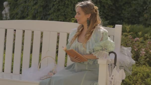 Girl on a bench reading a book in the afternoon in summer — Stock Video