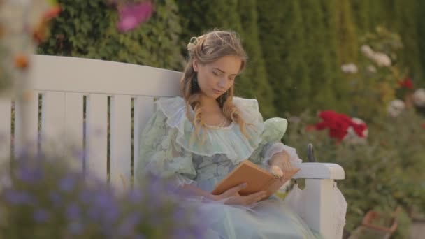 Menina em um banco lendo um livro à tarde no verão — Vídeo de Stock