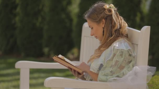 Κορίτσι σε ένα παγκάκι διαβάζοντας ένα βιβλίο το απόγευμα το καλοκαίρι — Αρχείο Βίντεο