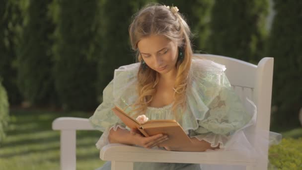 Menina em um banco lendo um livro à tarde no verão — Vídeo de Stock