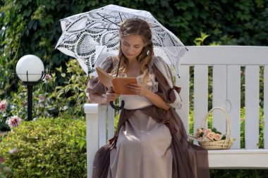 bir kitap ile beyaz bir bankta oturan kız