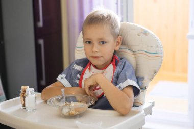 2020 'deki çocuk masasında önlüklü bir çocuk yulaf lapası yiyor.