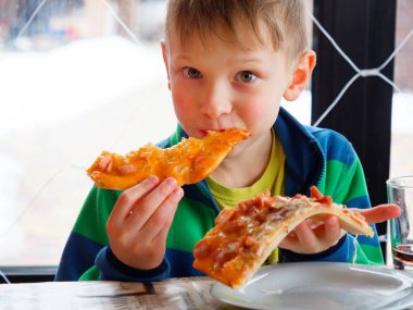 Açgözlülükle pizza yiyen bir çocuğun portresi.