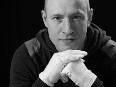 Siyah arka planda beyaz eldivenli kel bir adamın portresi.