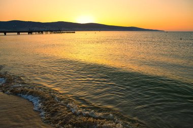 Renkli akşam bulutlu gökyüzünün altında durgun mavi deniz suyu.