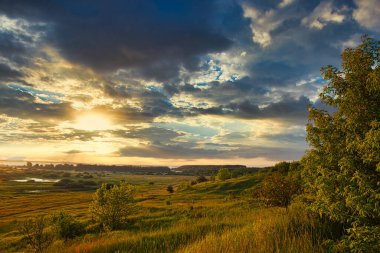 Bir nehrin üzerinde puslu bir gün doğumu ve üzerinde yol olan bir çimen tarlası. 2021