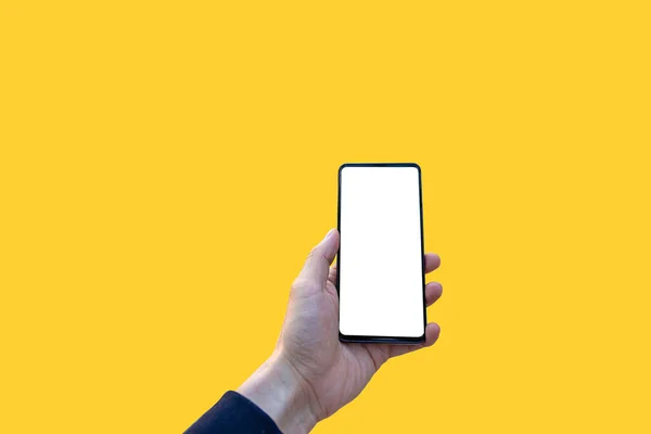 İzole edilmiş bir el, sarı arka planda boş ekranlı bir cep telefonu tutuyor.