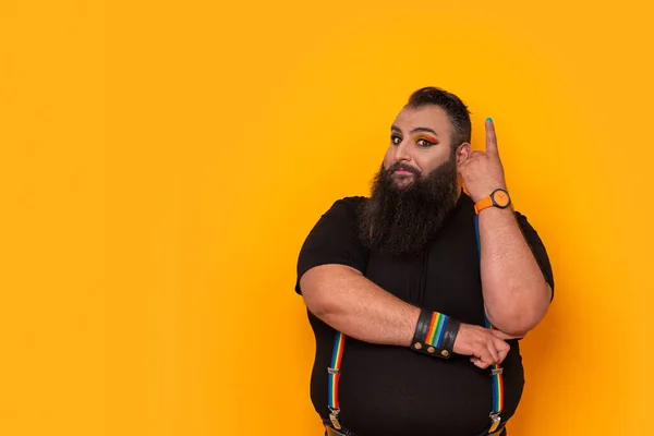 Bearded gay big man with rainbow trouser holder and make-up pointing up