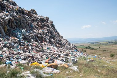Landfill near crop fields and small city. Enormous Trash wave near fields clipart