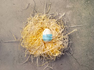 Yüz maskesi takan bir yumurta beton zeminde yuva yapıyor. Paskalya kutlamalarında yalnızlık kavramı karantina ve salgın yüzünden.