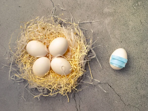 White Eggs laying in Nest. One egg wear in face mask laying at a distance outside nest.Concept of Outcast.