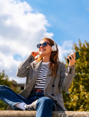 Kadın dışarıda kulaklıklarla müzik dinliyor.