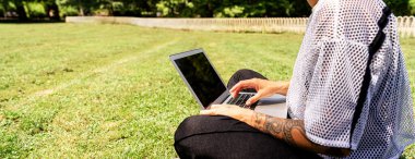 Çimlerin üzerinde oturan ve laptopunu kullanan şehirli kadın..