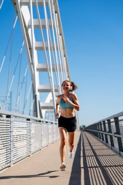 Şehir köprüsünde spor giyim ve kablosuz kulaklık takan genç bir kadın..