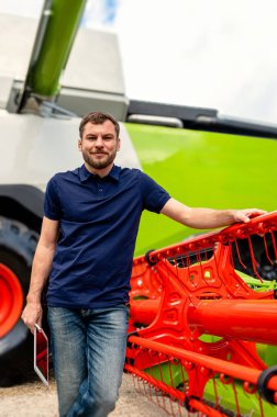 Bayilikte elinde tablet olan bir adam çiftlik makinelerinin yanında duruyor.