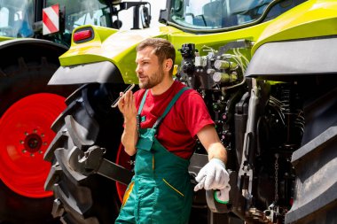 Tarım makineleri teknisyeni dışarıda traktörün yanında akıllı telefonunu kullanarak sesli mesaj kaydediyor.