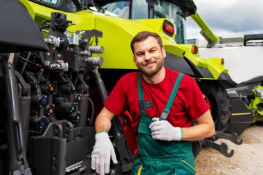 Traktörlerin yanında gülümseyen tarım işçisinin portresi.