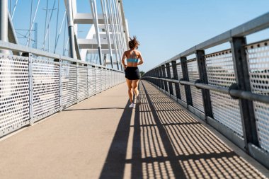 Back view of a female athlete running on the city bridge in summer.