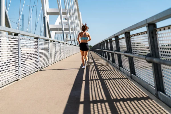 Back view of a female athlete running on the city bridge in summer.