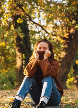 Sonbahar parkında rahat bir süveter giyen genç bir kadın.