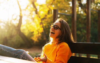 Genç bir kadın gülerek sonbahar parkında mola veriyor.