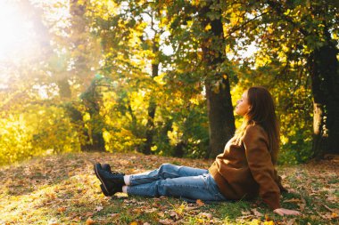 Huzurlu bir kadın sonbahar ağaçlarının arasında oturmuş, dışarıda sakin vakit geçiriyor..