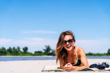 Güzel bir kadın güneşli yaz gününde kumlu sahilde dinleniyor.