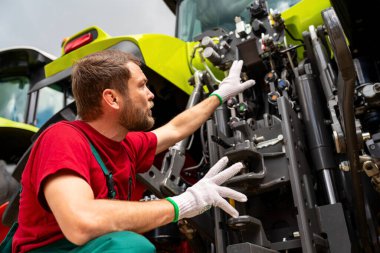 Tarımsal ekipman tamircisi traktörün bir kısmına işaret ediyor
