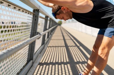 Yetişkin adam yazın şehir köprüsünde antrenmandan önce ısınma egzersizi yapıyor..