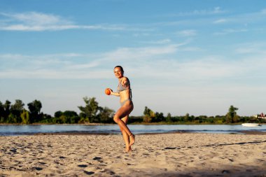 Yaz tatilinde kumsalda top atan aktif bir kadın.