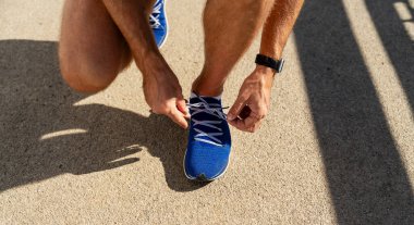 Koşmadan önce koşu ayakkabısı bağlayan erkek koşucunun yakın çekimi.