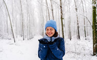 Genç bir kadın ormanda kışın kar yağışı seyrediyor. Eldivenlerindeki kar tanelerine bakan bir kadın..