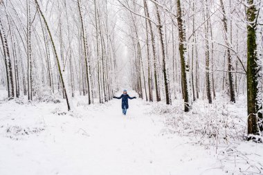 Neşeli genç kadın kışın karlı ormanda yürüyor.