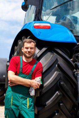 Açık havada traktöre yaslanmış gülümseyen erkek çiftçinin portresi.