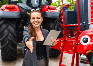 Tarım makineleri tarafından el sıkışma sunan tabletli kadın yönetici