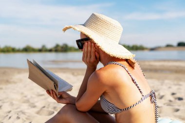 Güneşli sahilde kitap okuyan bir kadın..