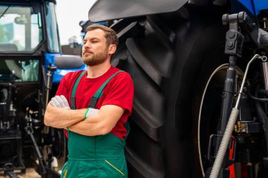 Çapraz kollu erkek tamirci traktörün yanında poz veriyor.