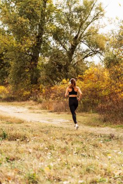 Sonbaharda açık havada koşan aktif bir kadının arka görüntüsü