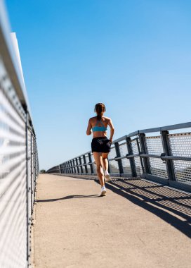 Kadın koşucu yazın şehir köprüsünde açık havada egzersiz yapıyor..