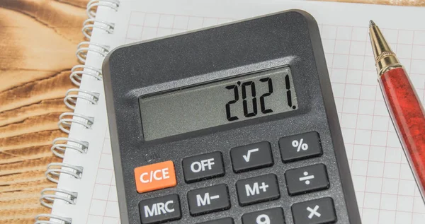 Black electronic calculator with 2021 lettering on the screen, paper Notepad and pen on a dark wooden background