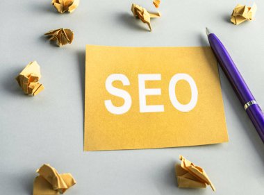 SEO-arama motoru optimizasyonu, sarı kare kağıttaki kelimeler, buruşmuş kağıtlar ve yakınlarda bir kalem var. Fikir, vizyon, strateji, analiz, anahtar sözcükler ve içerik kavramı