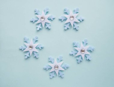 Mavi bir Noel arka planında keçeden ve yapay elmaslardan yapılmış şirin kar taneleri deseni, üst manzara, düz yatış, uzay kopyası.